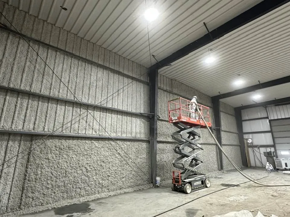 Worker on a scissor lift applying material to a warehouse interior wall.