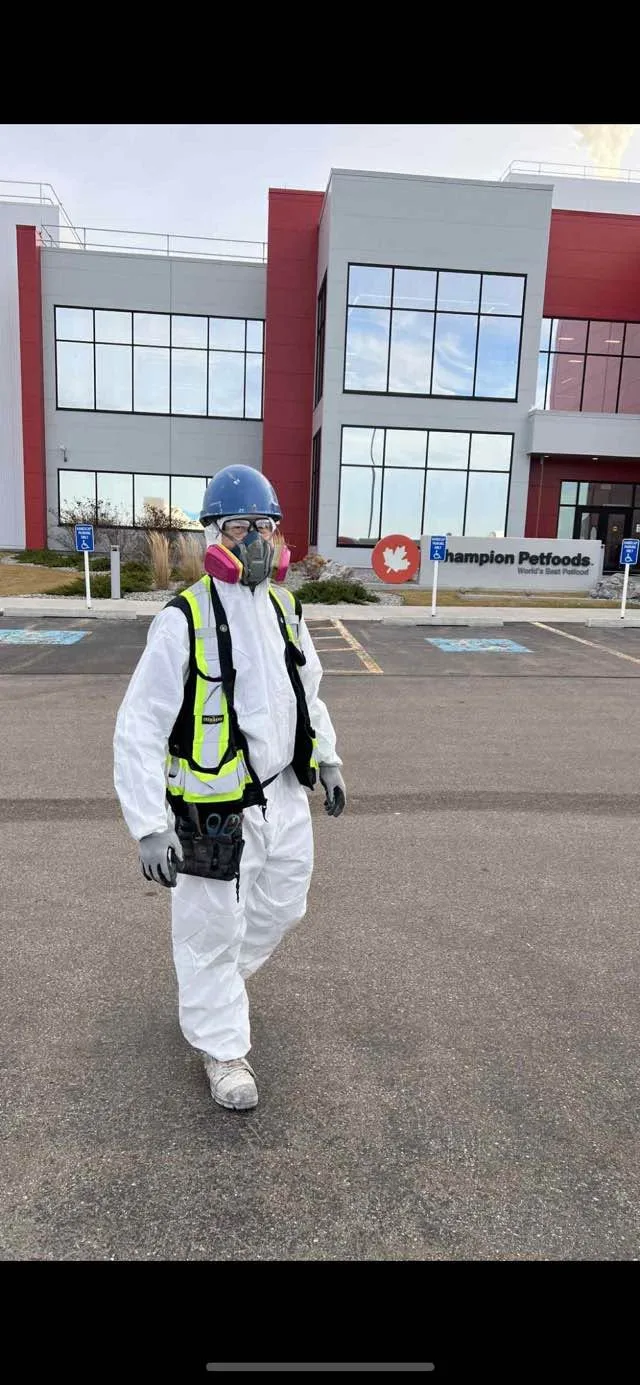 Person wearing a hard hat, respirator and protective clothing outside a building.